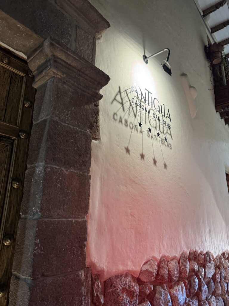 Illuminated sign for Antigua Casona San Blas in Cusco, Peru — five-star boutique hotel entrance with stone walls, wooden door, and shadowed lettering, marking a sacred arrival point for the starseed journey.