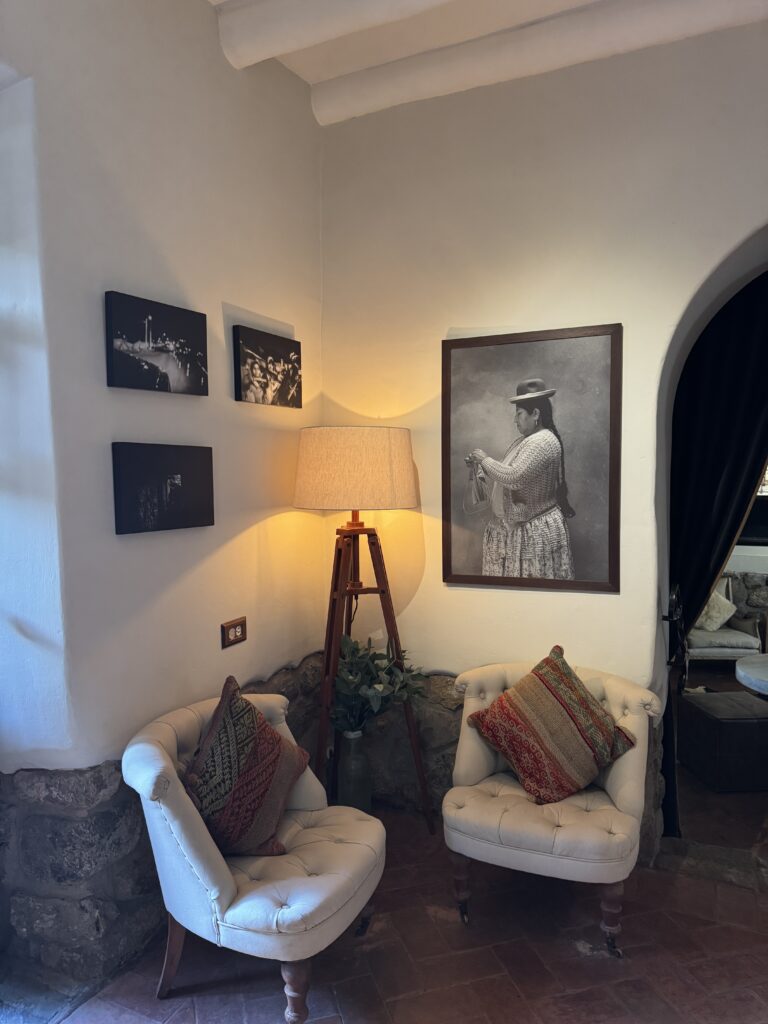 Two tufted armchairs with patterned pillows beside a warm lamp and framed cultural portraits — a quiet reflection corner at Antigua Casona in Cusco, Peru, where starseeds pause between sacred encounters.