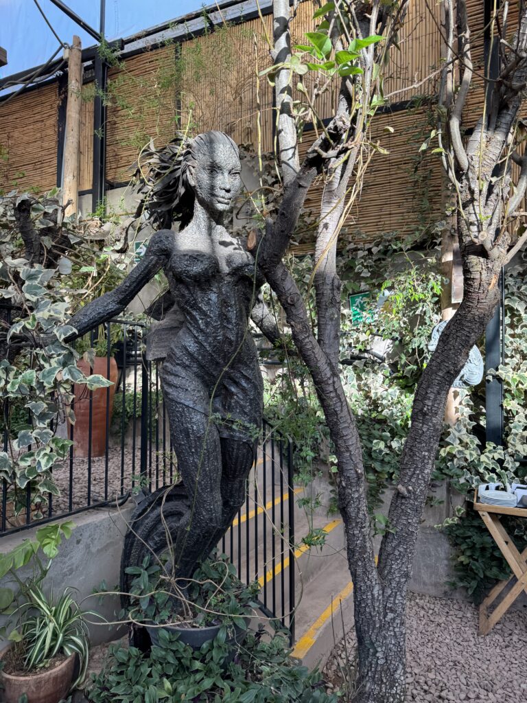 Sculpture of a human figure entwined with a tree in a lush garden at Green Point Vegan Restaurant in Cusco, Peru — a symbolic moment of starseed reflection, transformation, and unity with nature.