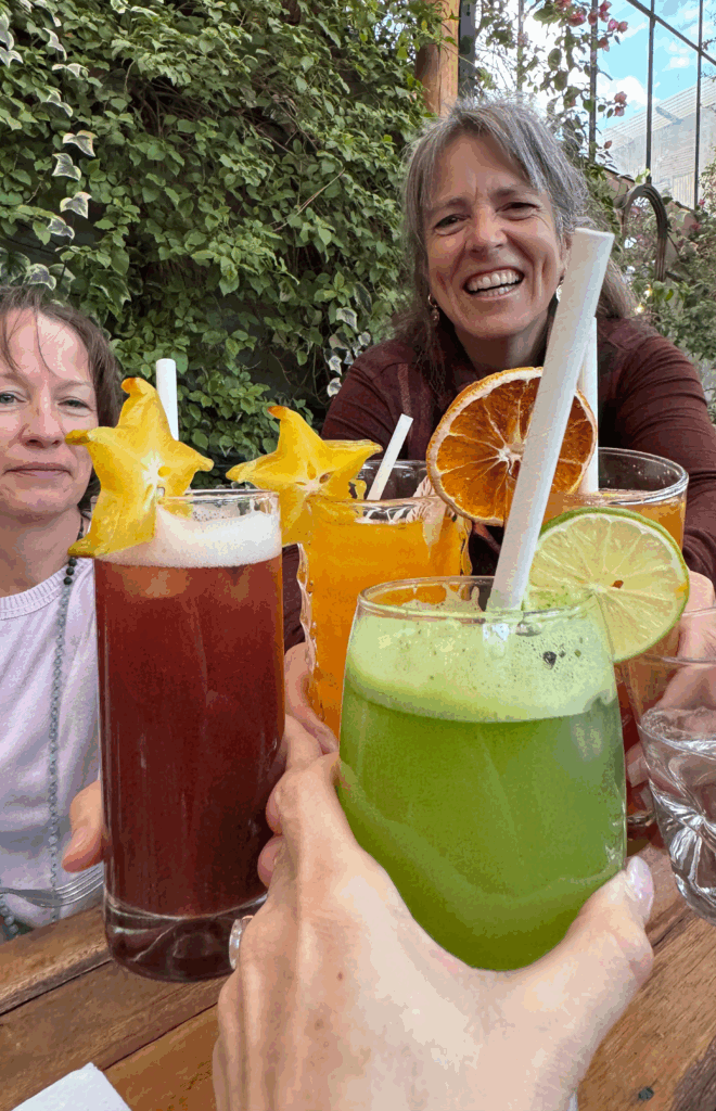 A group of starseeds raising colorful fruit-infused drinks in a joyful toast at Green Point Vegan Restaurant in Cusco, Peru — celebrating connection, vitality, and the spirit of the journey.