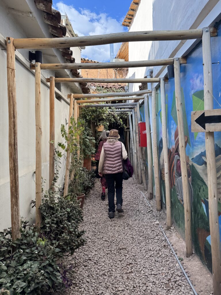 Two starseeds walking along a mural-lined pathway toward Green Point Vegan Restaurant in Cusco, Peru — entering the space for a shared meal and connection.