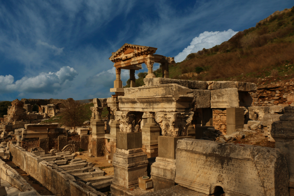 Collective Memory embodied in the ornate funerary monuments of ancient Ephesus, where elaborately carved stone sarcophagi, Corinthian capitals, and a restored temple-like tomb rise among the ruins beneath a dramatic Anatolian sky. Photographed during the Starseed Türkiye Adventure with Althea Provost, the archaeological landscape preserves inscriptions, craftsmanship, and enduring cultural memory from one of the most important cities of the ancient Mediterranean.
